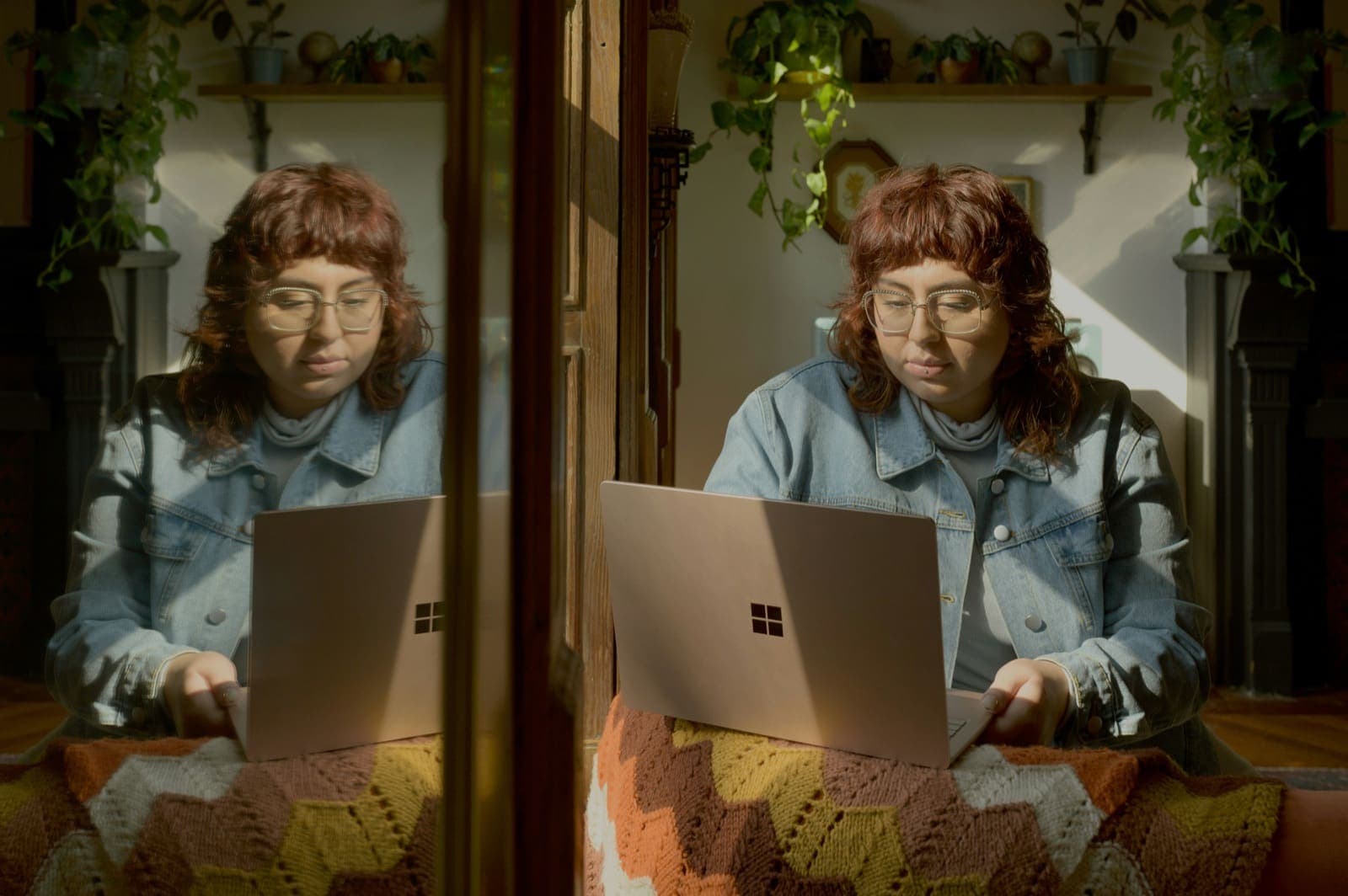 An adult working on a laptop by a sunny window, reflected in the glass