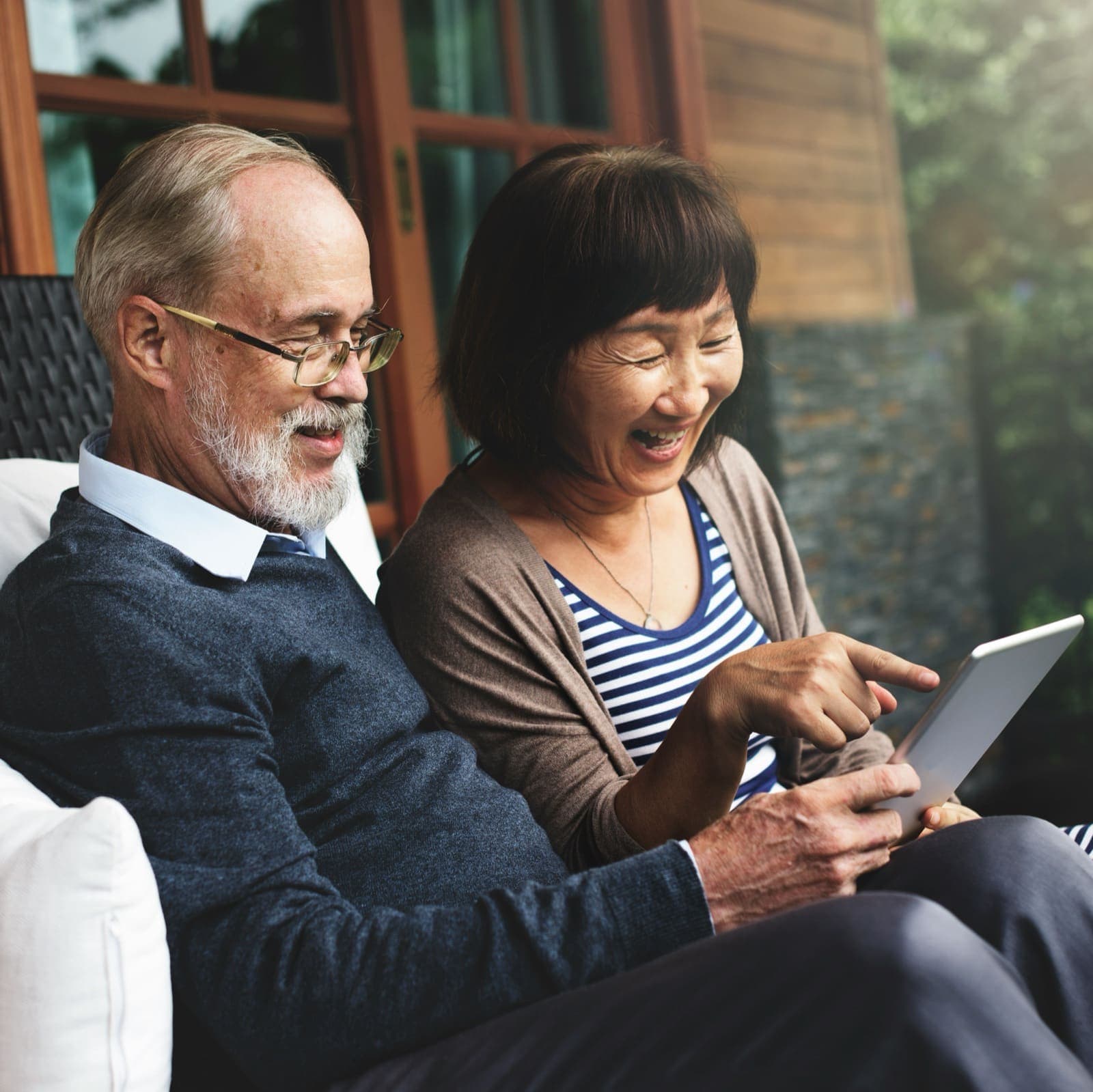 Two adults smiling together over a tablet on a couch