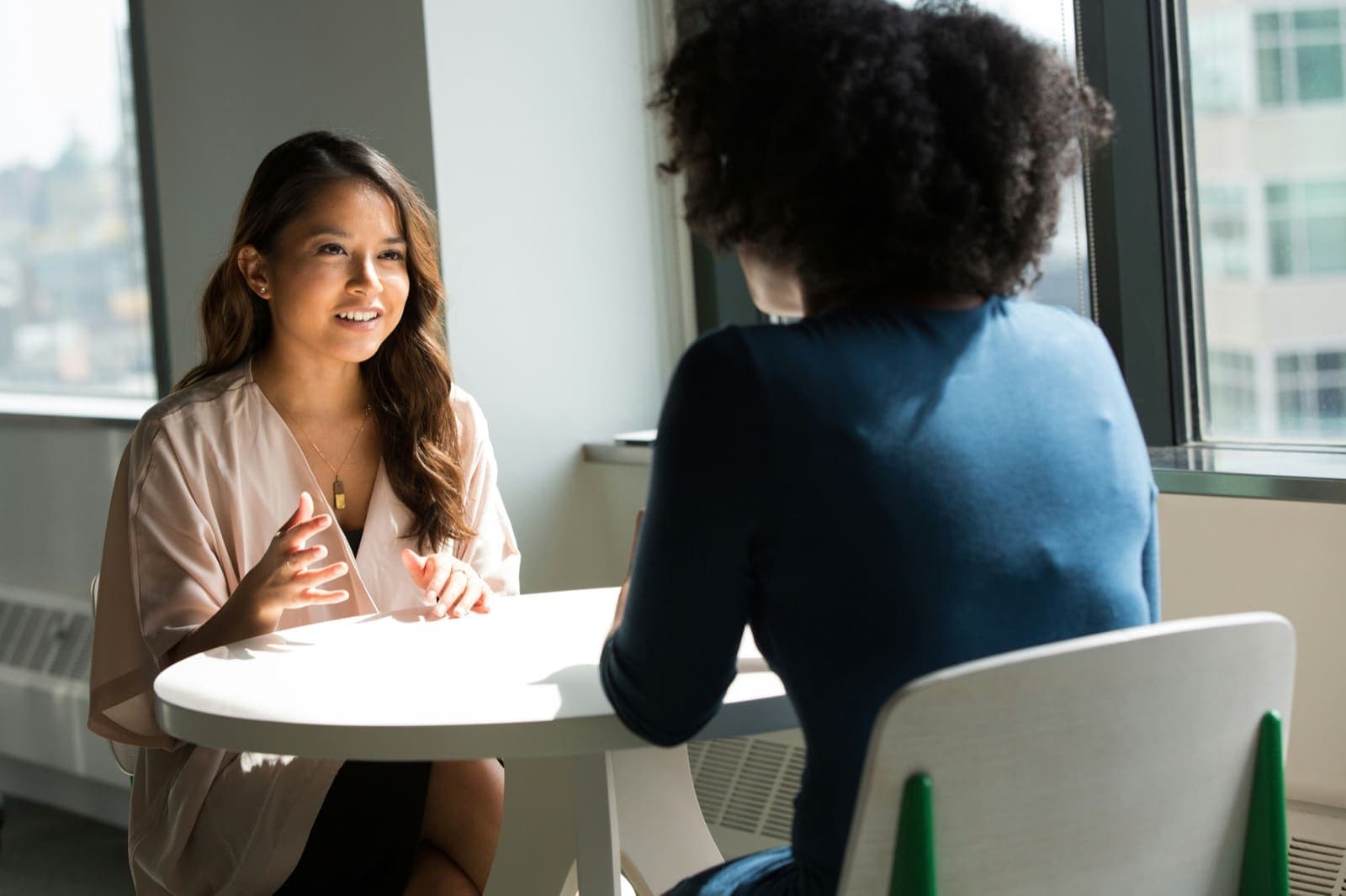 Two people in conversation across a small table by a bright office window