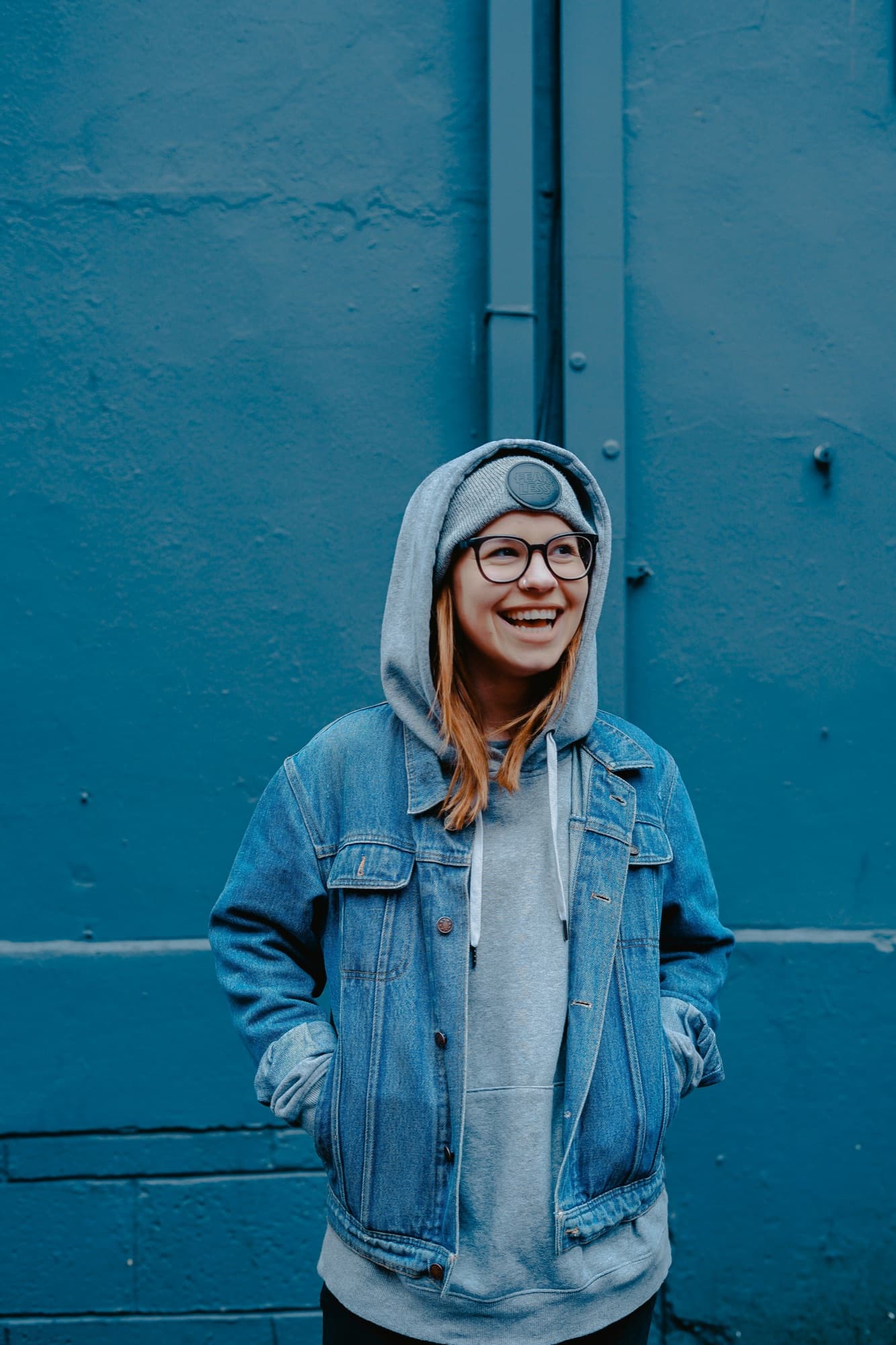 A teen in a denim jacket smiling against a blue wall